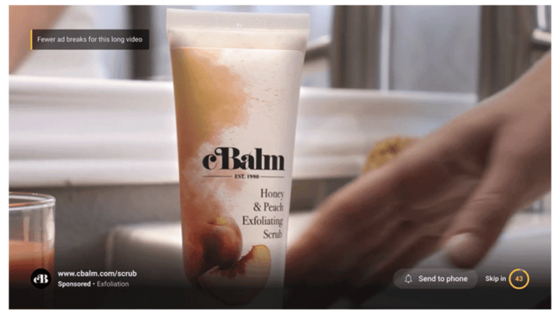 A tube labeled "eBalm Honey & Peach Exfoliating Scrub" is displayed on a bathroom counter, evoking a smooth streaming experience for your skin. A hand reaches toward it, beside a mirror and small jar. On-screen buttons and a sponsored link are visible at the bottom.