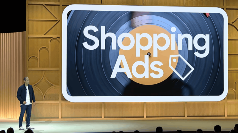 A person stands on stage next to a large screen displaying "Shopping Ads" with a stylized record graphic in the background, hinting at new features. The setting appears to be a presentation or talk, possibly at GML 2024.