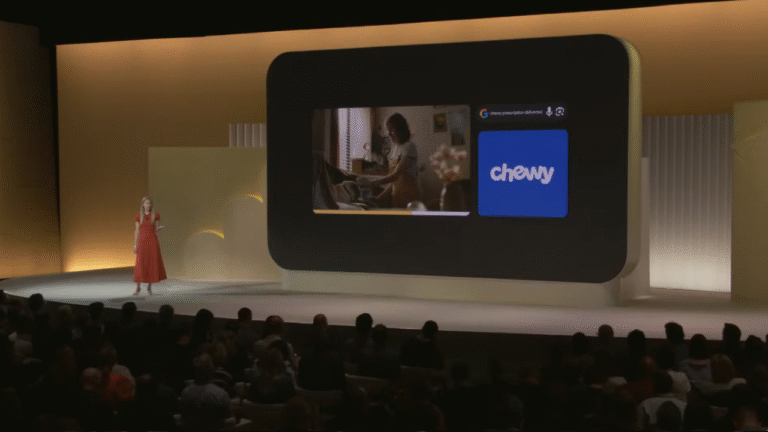 A woman in a red dress presents onstage to an audience, standing beside a large screen displaying an image of a person with a cat and the Chewy logo.