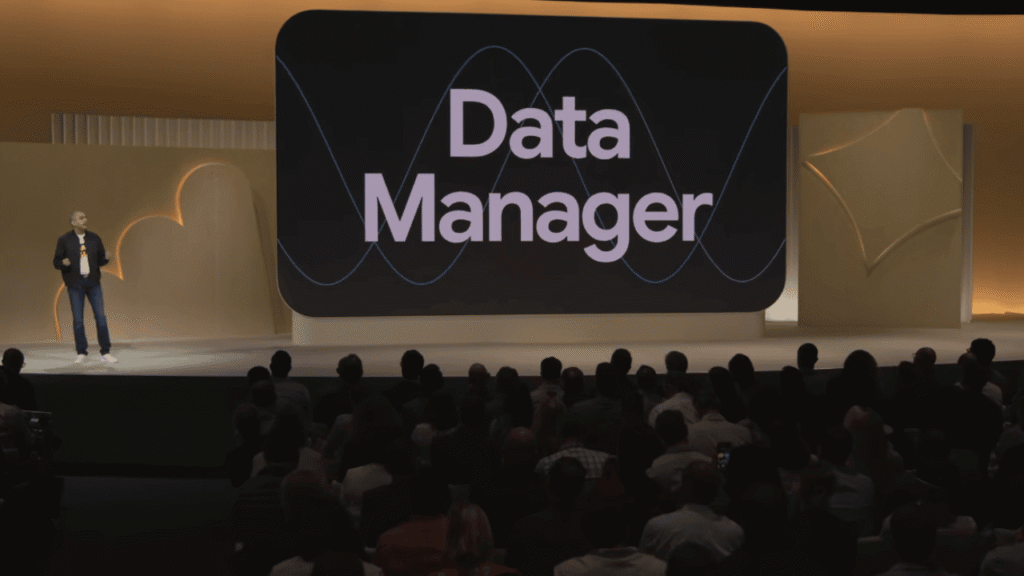 A speaker stands on stage in front of an audience at GML 2025, presenting a large screen that displays the words "Data Manager" with abstract wave graphics, highlighting the importance of data integration.