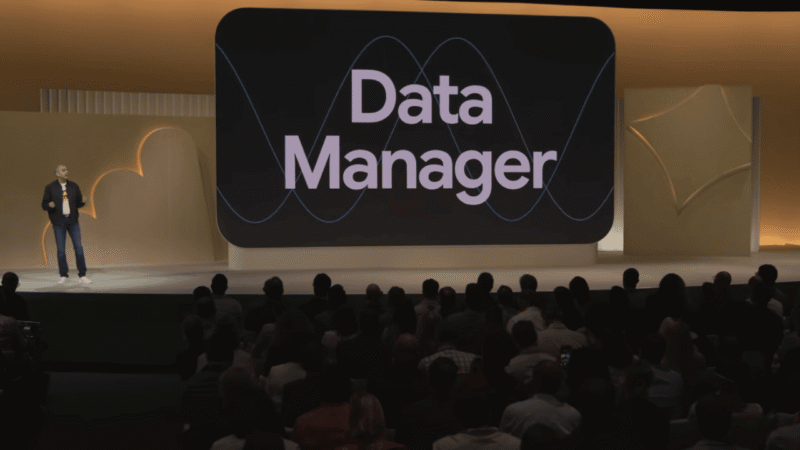 A speaker stands on stage in front of an audience at GML 2025, presenting a large screen that displays the words "Data Manager" with abstract wave graphics, highlighting the importance of data integration.