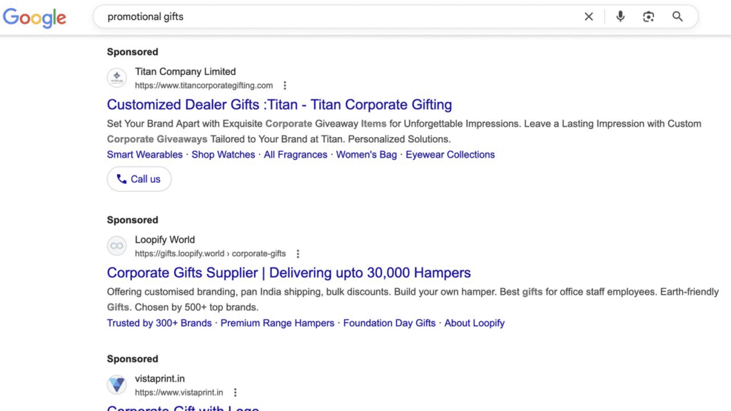 Google search results page for "promotional gifts," showing sponsored links for Titan Company, Loopify World, and Valueprint.in, each offering customized corporate gifting and hampers. The search bar appears at the top.