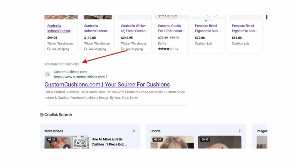 A Google search results page displays a Search Ads label on an ad for "CustomCushions.com | Your Source For Cushions," highlighted by a red arrow. Various shopping links and product listings appear above the ad.