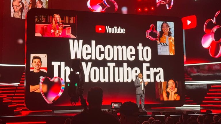 A presenter stands on stage in front of a large screen displaying "Welcome to The YouTube Era" with the YouTube logo, surrounded by neon red lighting and images of content creators on a dark background.